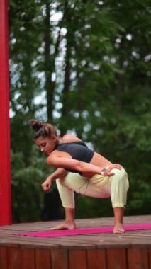Genç bir kadın sabah tahta bir podyumda yoga yapıyor.