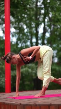 Genç bir kadın sabah tahta bir podyumda yoga yapıyor.