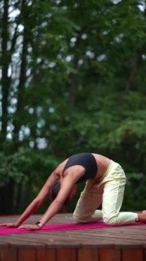 Genç bir kadın sabah tahta bir podyumda yoga yapıyor.