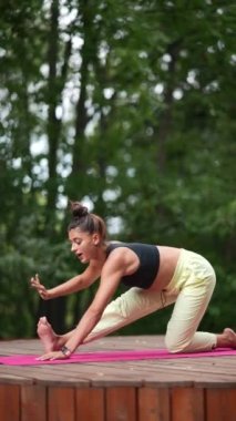 Genç bir kadın sabah tahta bir podyumda yoga yapıyor.