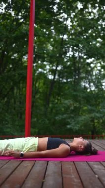 Genç bir kadın sabah tahta bir podyumda yoga yapıyor.