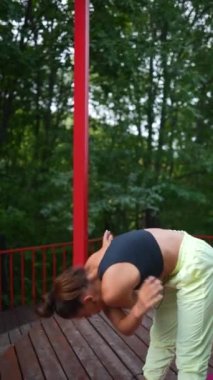 Genç bir kadın sabah tahta bir podyumda yoga yapıyor.