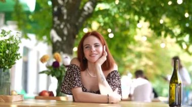 Genç ve güzel bir kız bir kafede otururken kameraya konuşuyor.