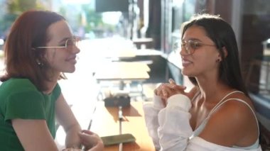 İki güzel kız arkadaş şehirde bir barda otururken konuşuyor.