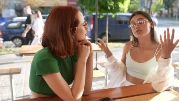 两个漂亮的女朋友坐在城市街上的酒吧里聊天 — 图库视频影像