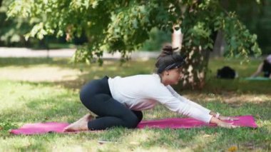 Bir grup genç spor kadın parkta eğitmenle yoga dersi veriyor.