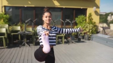 Spor kıyafetli genç, mutlu bir kadın sabahın erken saatlerinde evin çatısında yoga minderinde esneme egzersizleri yapıyor.