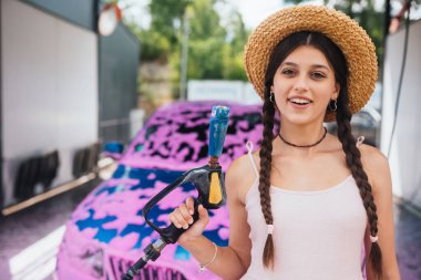 Genç kadın yüksek basınçlı hortum pembe köpükle kaplı bir arabanın önünde duruyor.