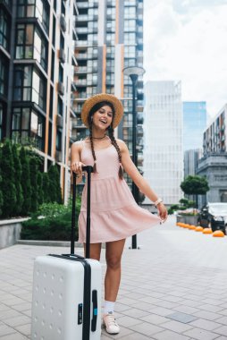 Modern bir şehrin arka planında bavulu olan güzel bir kadın.