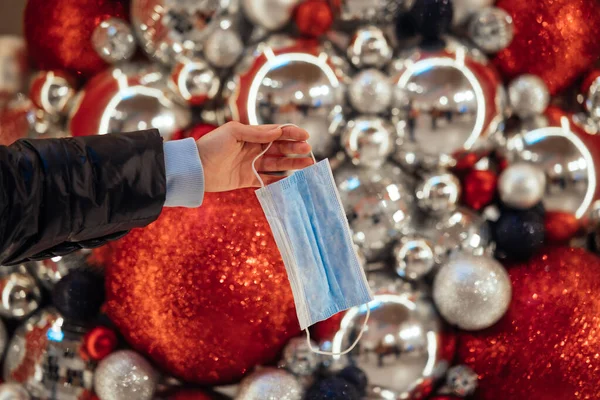 A female hand is holding a medical mask on the background of Christmas balls