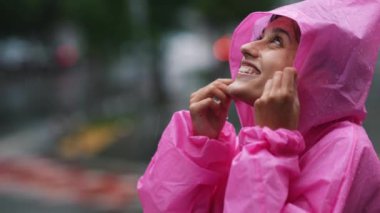 Young smiling woman with a pink raincoat on the street while enjoying a walk through the city on a rainy day.