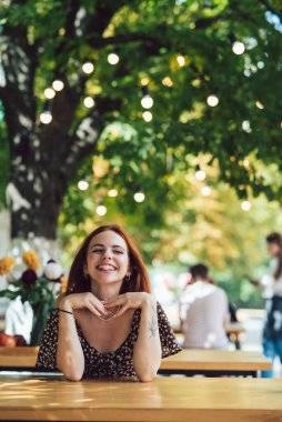 Arka plandaki yazlık kafede terasta kahve içen iki kız arkadaşın yakın plan portresi.