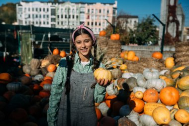 Küçük balkabaklı genç bayan satıcı sonbahar hasadı arasında kameraya poz veriyor. Tarım kavramı.