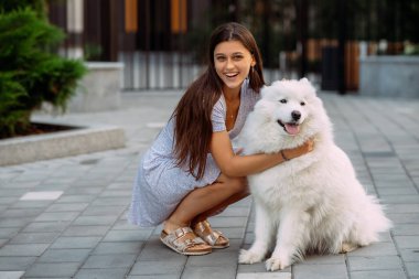 Genç bir kadın yazın gün batımında büyük bir köpeğe sarılır.