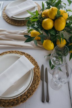 Düğün partisindeki şenlik masası limon aranjmanıyla süslenmiştir. Masanın üstünde peçete ve gözlüklerle dolu tabaklar vardır.