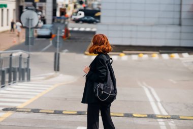 Sırt çantalı, gülümseyen mutlu genç bir kadın yolda dikilirken kameraya poz veriyor.
