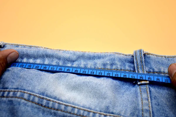 Jeans with blue tape measure hand on orange background. Waist measurement concept. Fat, skinny. Tailor.