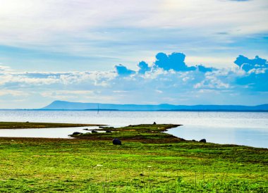 lake scenery  There is a mound covered with green grass.  A distant mountain near the horizon where black rain clouds were forming in the  day with inclement weather