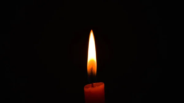 Burning orange candle flame in darkness copy space concept peace hope religion serenity