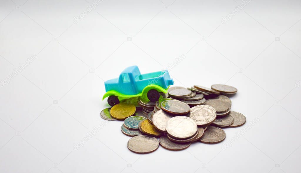 A blue-green pickup truck climbs on a pile of coins on a white background.