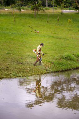 Uygun ekipmanlarla gölün kenarında çim biçen bir işçi..