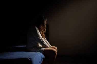 Kafası aşağıda, depresif bir şekilde, karanlık bir odada yatağın kenarında oturan bir kadın..