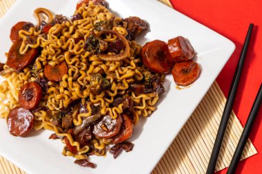 Soya soslu bir porsiyon sebze yakisoba ile beyaz bir yemek tabağı. Kırmızı bir tabağın içinde vejetaryen yakisoba..