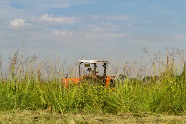Arka planda gökyüzü olan, çimlerin ortasında çalışan bir traktör..