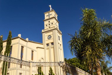 The side view of the Bom Jesus da Lapa Cathedral in the city of Anpolis with trees around it and blue sky in the background.