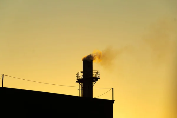 Smoke coming out of the factory chimney. Air pollution by smoke coming out of a factory chimney with the golden dawn sky.