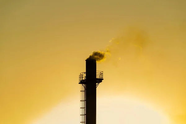 Smoke coming out of the factory chimney. Air pollution by smoke coming out of a factory chimney with the golden dawn sky.