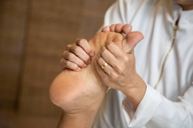 Closeup of massage therapist hands applying therapeutic massage to a patient's foot.