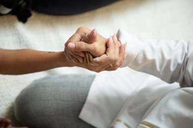 Closeup of hands of masseuse, who is kneeling on the floor, applying therapeutic massage on the hand of a patient who is lying down.