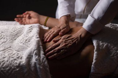 Closeup of massage therapist hands applying therapeutic massage on a patient's belly.