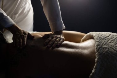 Detail of a massage therapist massaging the back of a patient who is lying on a stretcher.