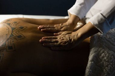 Detail of a massage therapist massaging the back of a patient who is lying on a stretcher.