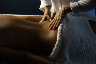 Detail of a massage therapist massaging the back of a patient who is lying on a stretcher.