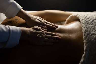 Detail of a massage therapist massaging the back of a patient who is lying on a stretcher.