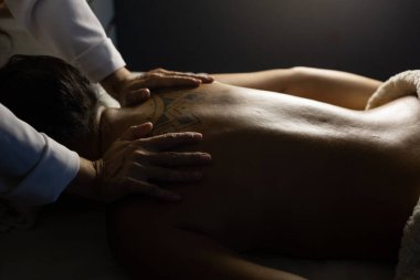 Detail of a massage therapist massaging the back of a patient who is lying on a stretcher.