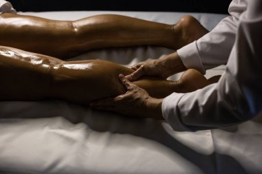 A therapist dressed in white, massaging the leg of a patient lying on a stretcher, using therapeutic oil.
