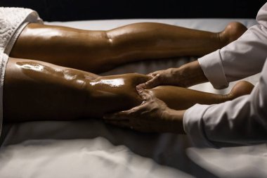 A therapist dressed in white, massaging the leg of a patient lying on a stretcher, using therapeutic oil.