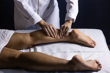 A therapist dressed in white, massaging the leg of a patient lying on a stretcher.