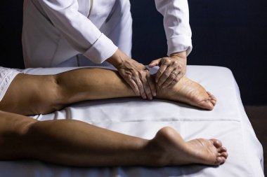 A therapist dressed in white, massaging the leg of a patient lying on a stretcher.