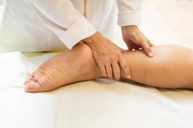 A therapist dressed in white, massaging the leg of a patient lying on a stretcher.
