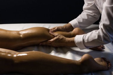 A therapist dressed in white, massaging the leg of a patient lying on a stretcher, using therapeutic oil.