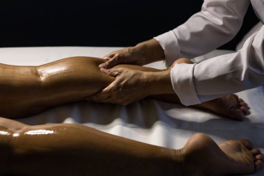 A therapist dressed in white, massaging the leg of a patient lying on a stretcher, using therapeutic oil.
