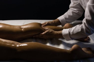 A therapist dressed in white, massaging the leg of a patient lying on a stretcher, using therapeutic oil.
