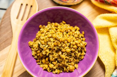 A crockery bowl with brown rice and lentils on a wooden surface, with a wooden spoon and a yellow cloth in the background.