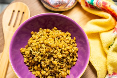 A crockery bowl with brown rice and lentils on a wooden surface, with a wooden spoon and a yellow cloth in the background.