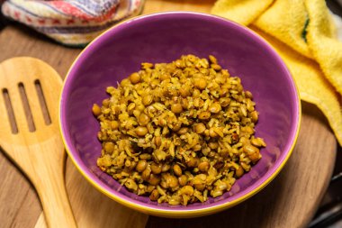 A crockery bowl with brown rice and lentils on a wooden surface, with a wooden spoon and a yellow cloth in the background.